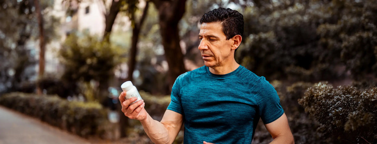 A man jogging outdoors in a blue athletic t-shirt while holding a white bottle in his hand, with trees and hedges blurred in the background.