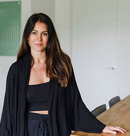 Woman in a black outfit standing indoors with a neutral background