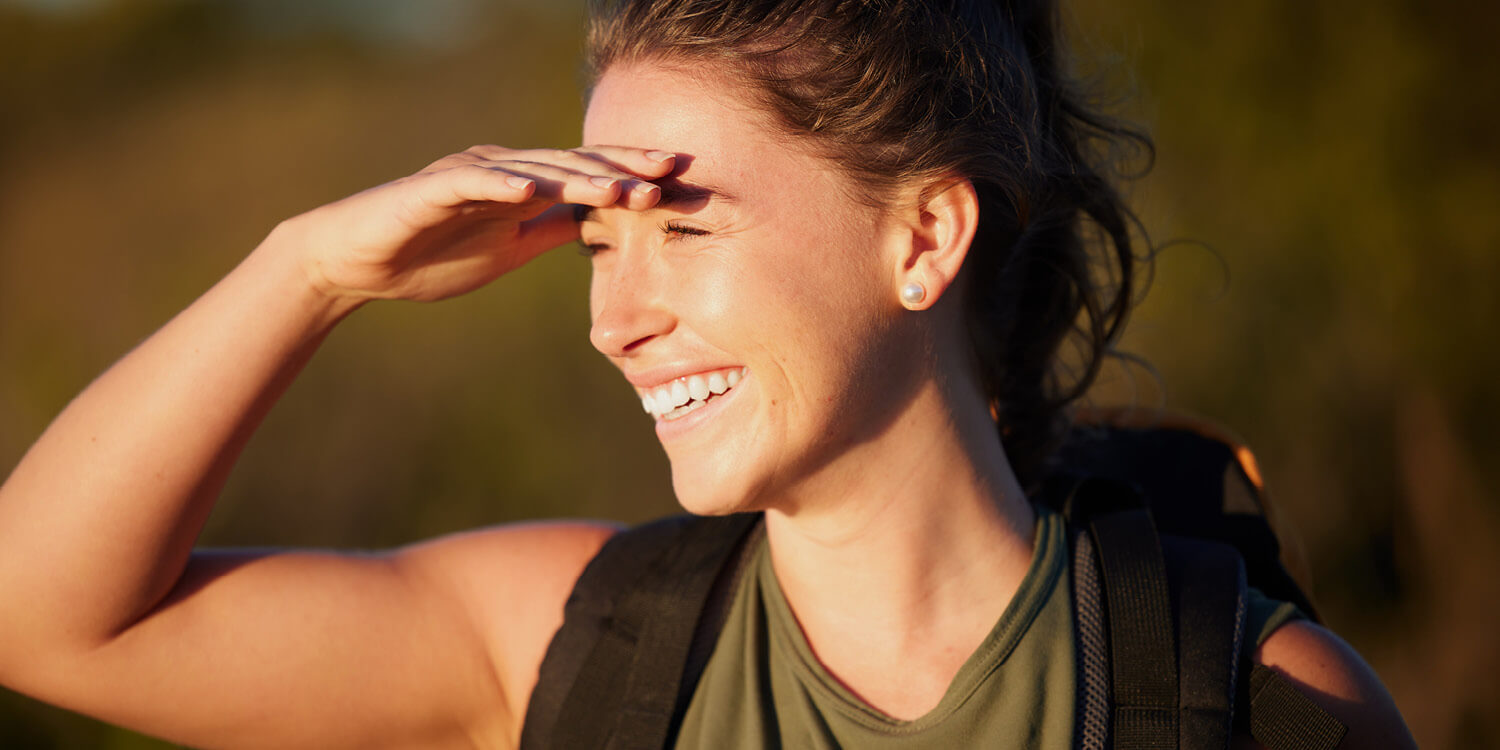 Woman blocking the sun with her hand against a blurred green background.