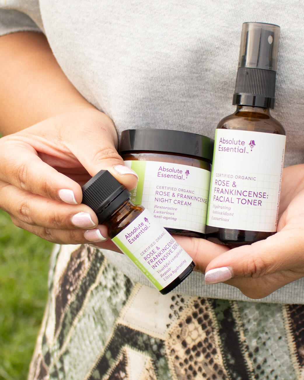 Hands holding Absolute Essential skincare products outdoors