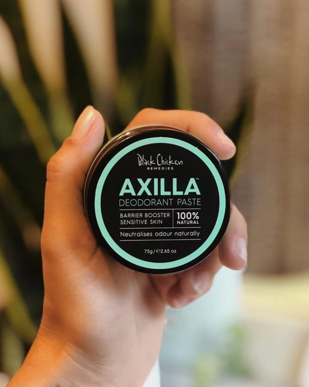 Hand holding a container of Axilla deodorant paste with a blurred background