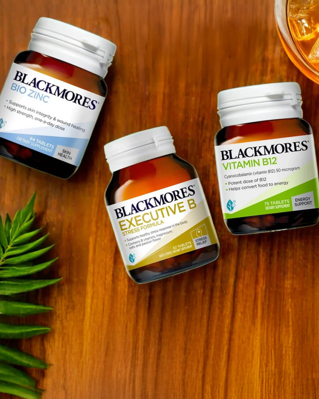 Three Blackmores vitamin bottles on a wooden surface with a glass of orange juice.