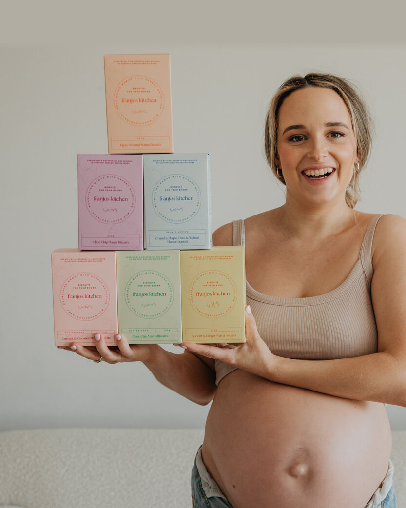 Pregnant woman holding five colourful boxes with a neutral background.