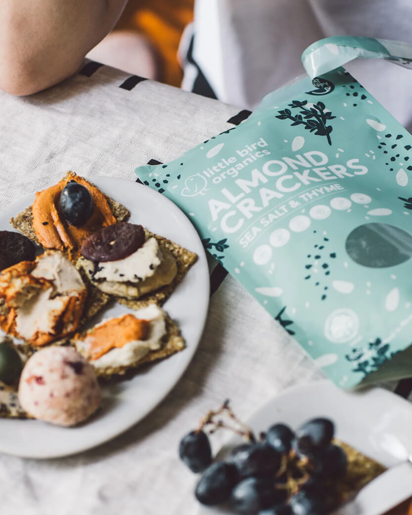Almond crackers on a plate with a package of Little Bird Organics almond crackers next to them.