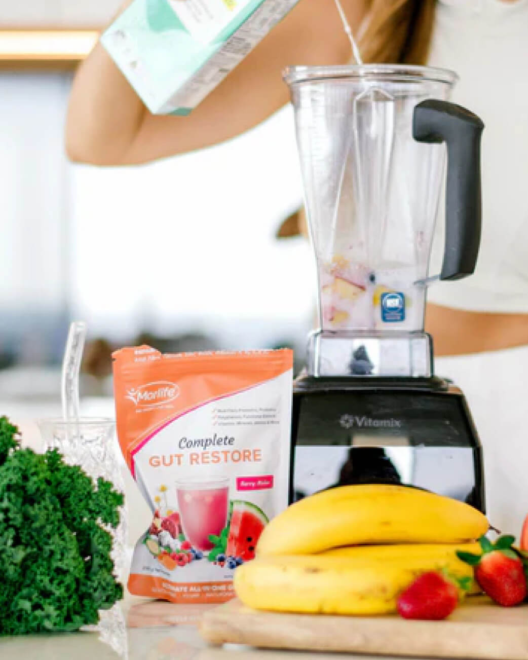 Blender with ingredients on a counter, including a package of 'Complete Gut Restore' and fruits.