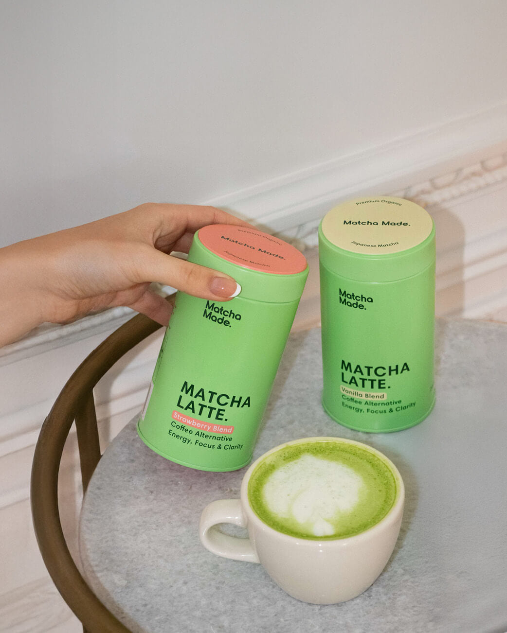 Matcha Latte containers with a cup of matcha latte on a table.