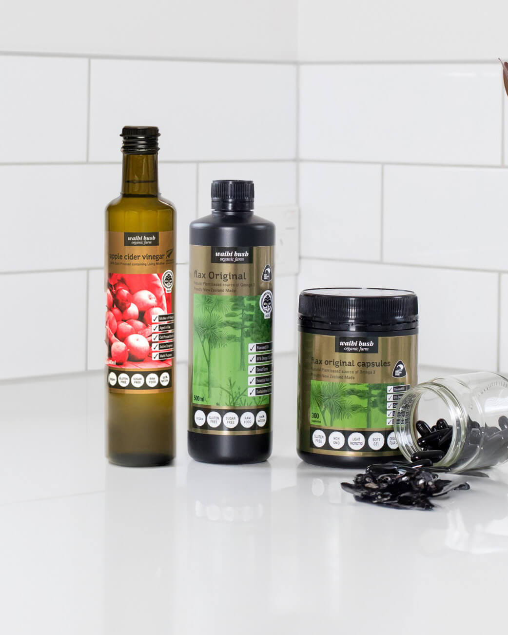 Three bottles and a jar of health products on a white surface with a tiled wall background.