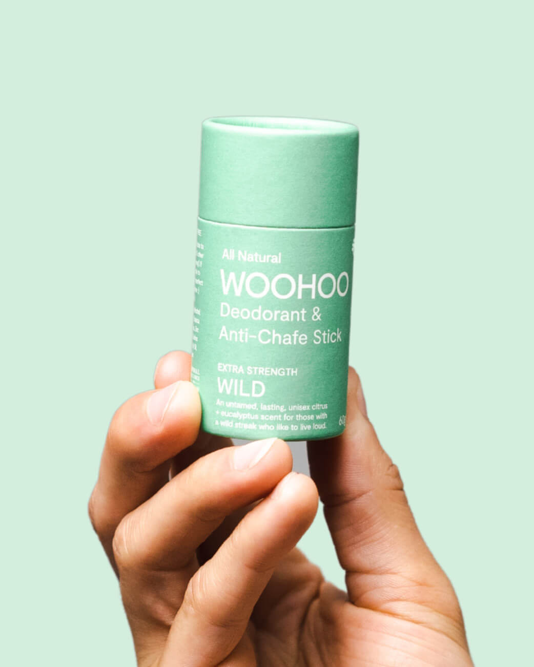 Hand holding a green deodorant stick with 'WOOHOO' branding against a light green background.