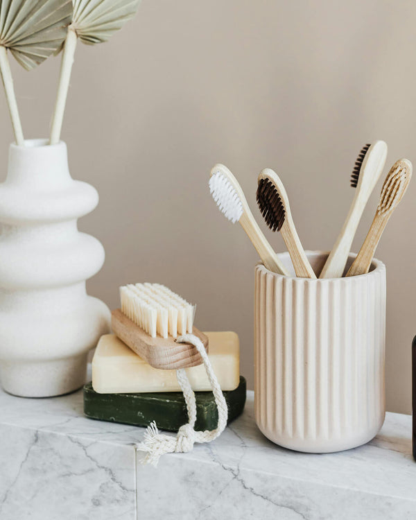 Set of bamboo toothbrushes in a ceramic holder on a marble surface with a neutral background.