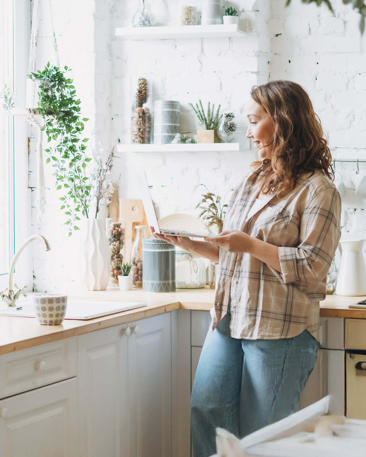 Woman standing in a kitchen holding a laptop.