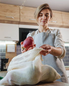 Woman in a kitchen holding an apple and a reusable mesh bag