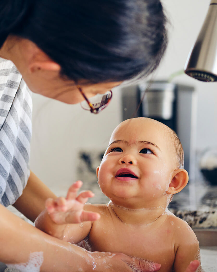 Baby being bathed by an adult in a bathroom setting.