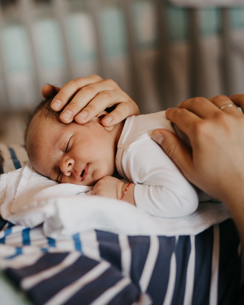 Newborn baby being comforted by an adult hand on a striped blanket