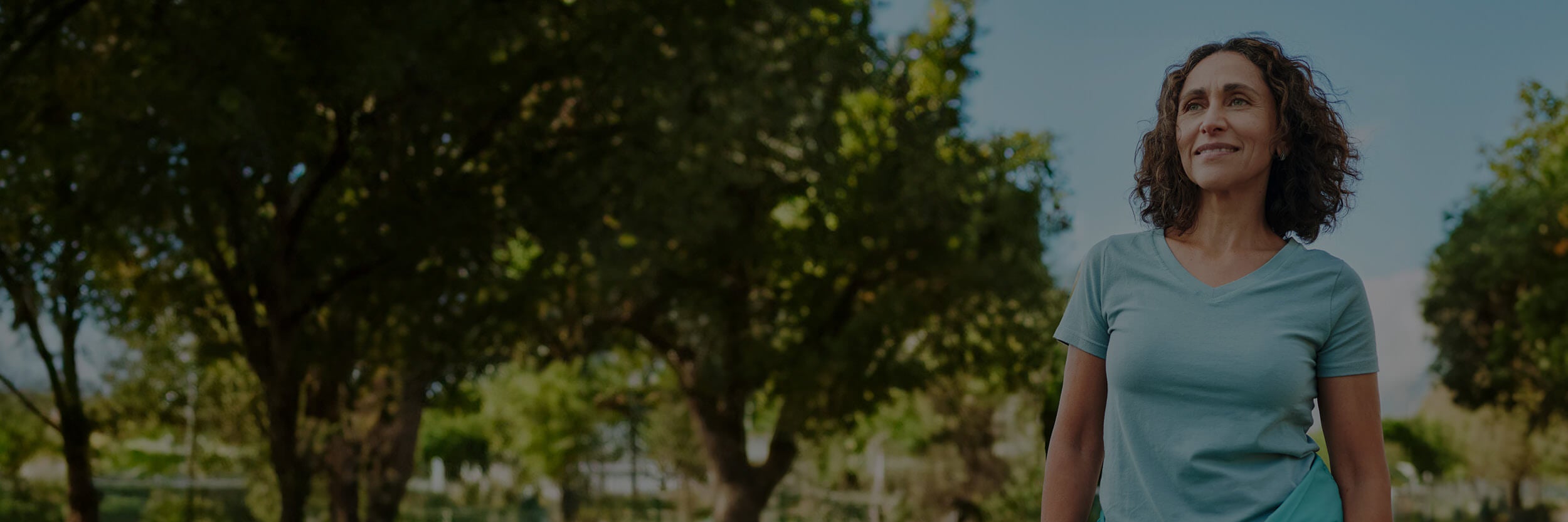 Woman wearing a blue shirt in an outdoor setting with trees in the background.