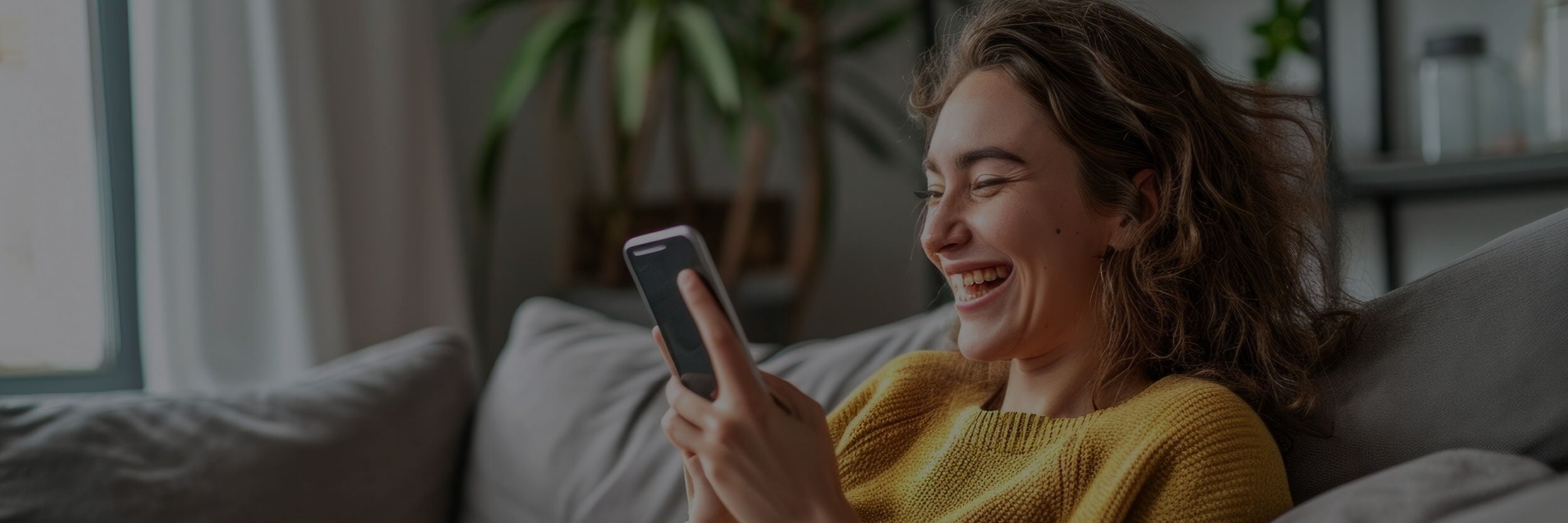 Woman sitting on a couch smiling at her phone.