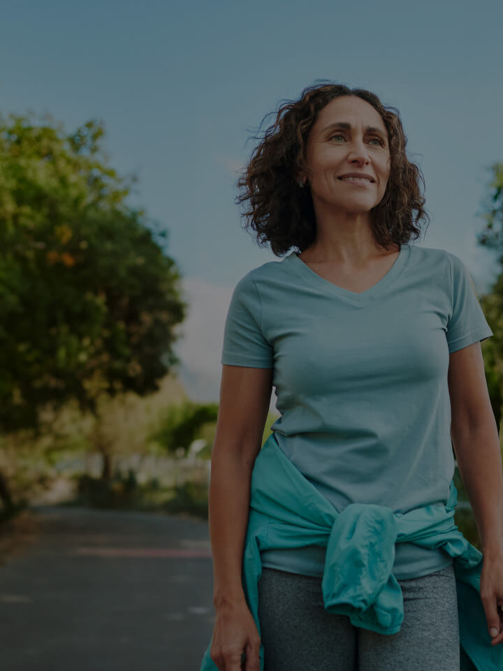 Woman in a teal shirt standing outdoors with trees in the background