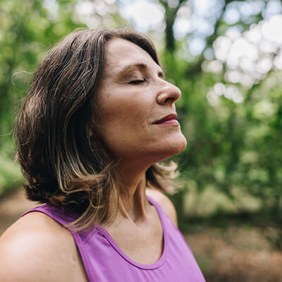 Woman in a purple tank top standing outdoors with trees in the background.