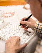 Person solving a crossword puzzle with a pen.