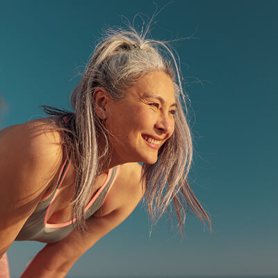 Woman with gray hair smiling outdoors against a blue sky.