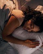 Person lying in bed with a pillow, surrounded by soft bedding.