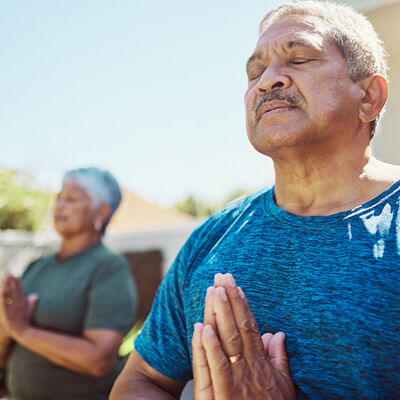 Man in a blue shirt meditating with another person in the background.