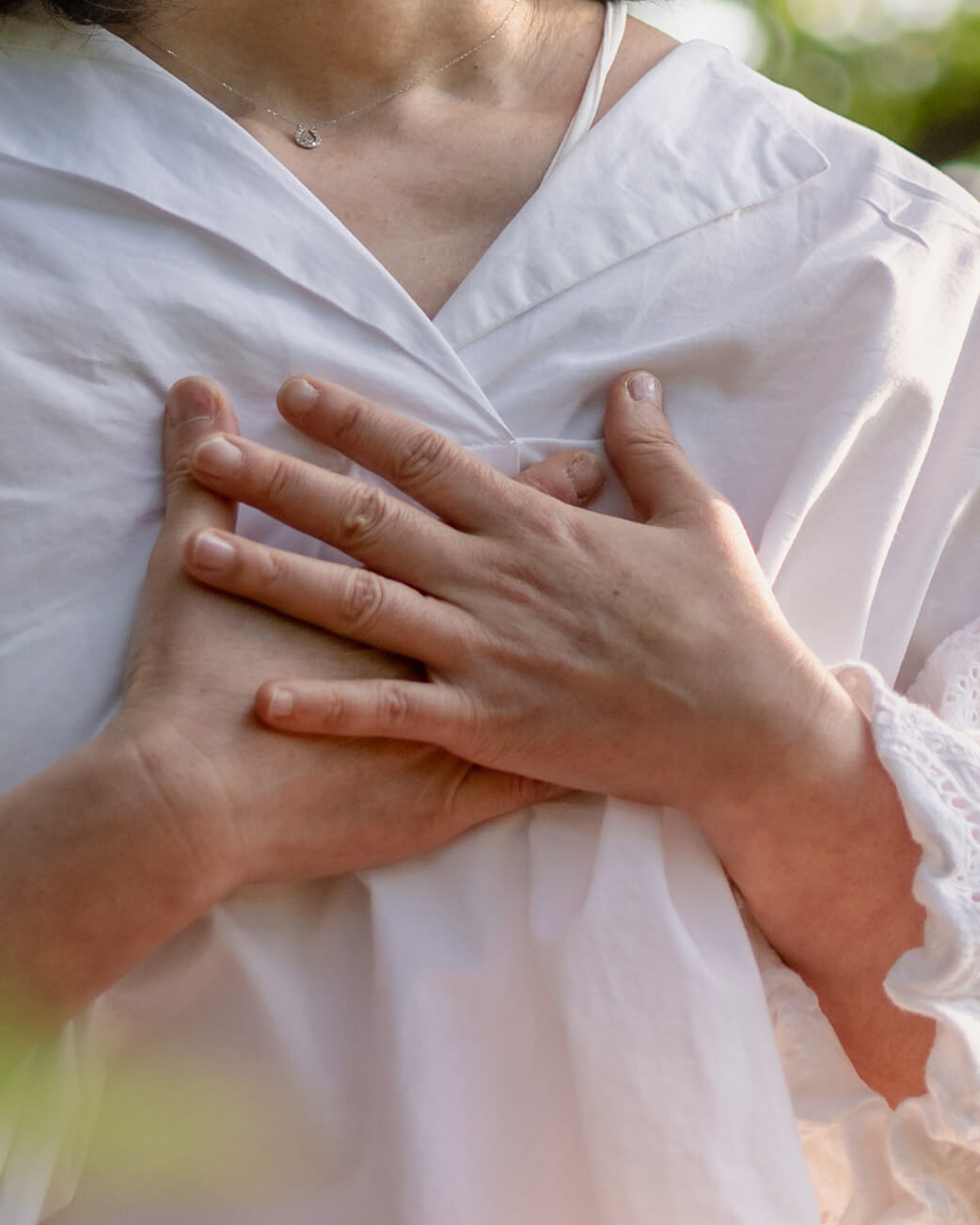 Close-up of hands resting on a white garment with a blurred natural background.