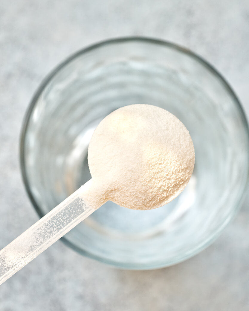 Spoonful of protein powder over a glass bowl on a light background