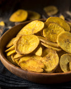 Bowl of dried plantain chips on a dark background.