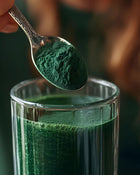Spoonful of green powder being added to a glass of green liquid
