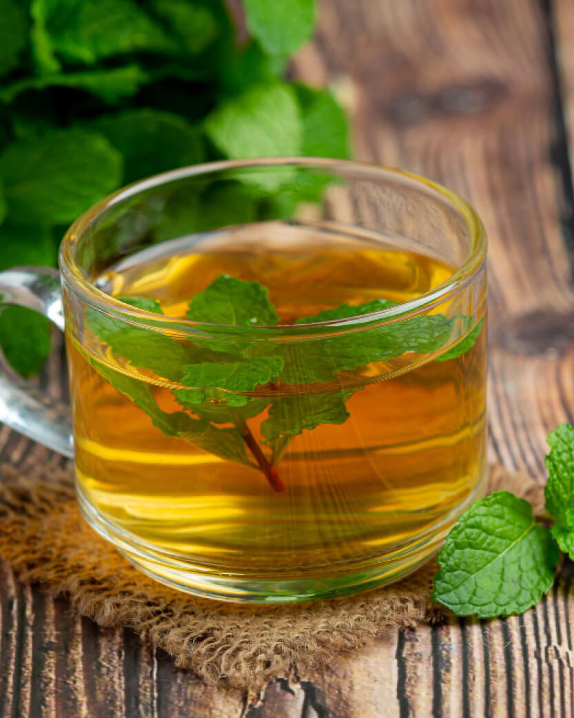 Clear glass mug filled with green tea and mint leaves on a wooden surface.