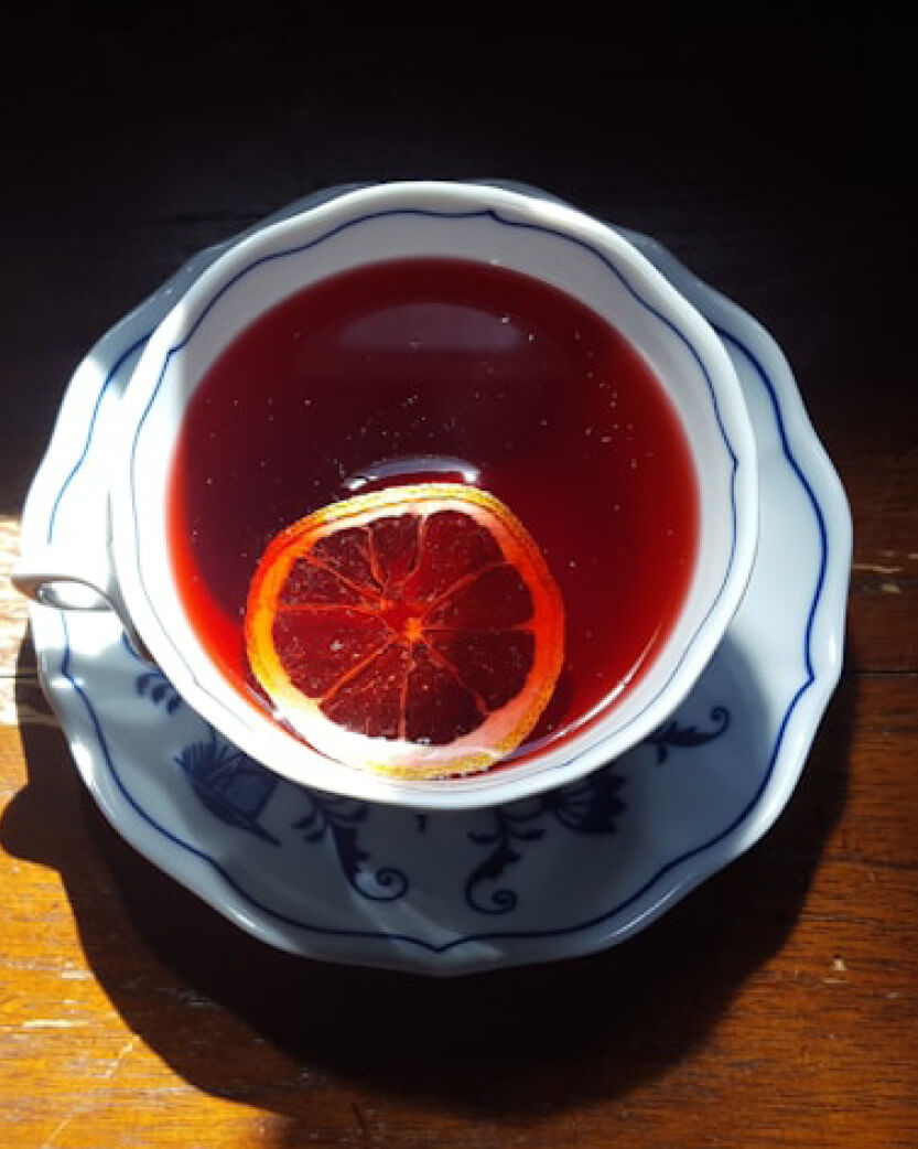 Teacup with red bush tea and orange slice on a wooden surface