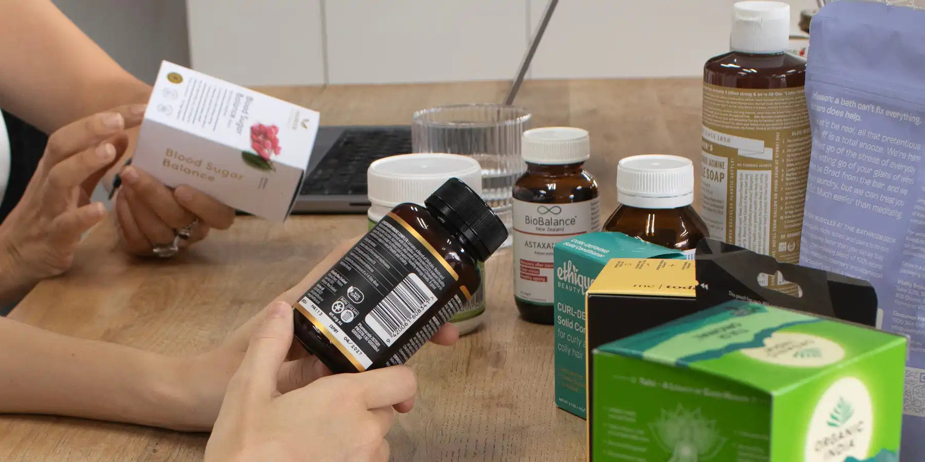 Person examining a bottle of supplements with various health products on a table.