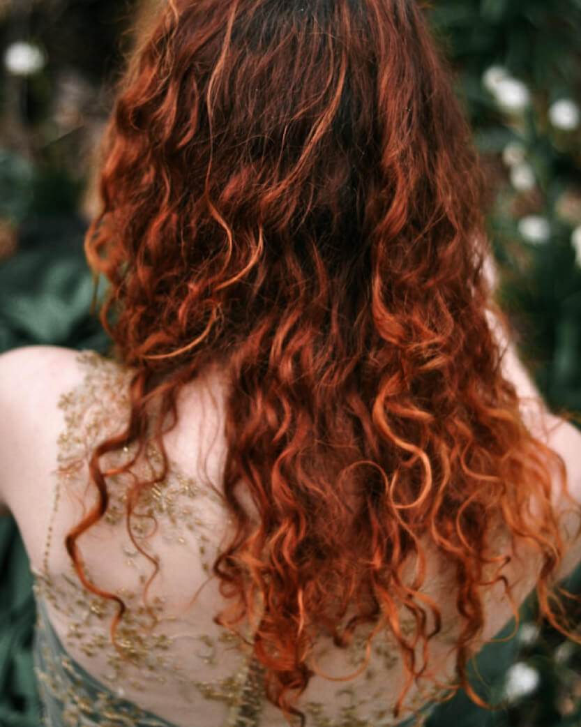 Person with long, wavy red hair with a blurred natural background.