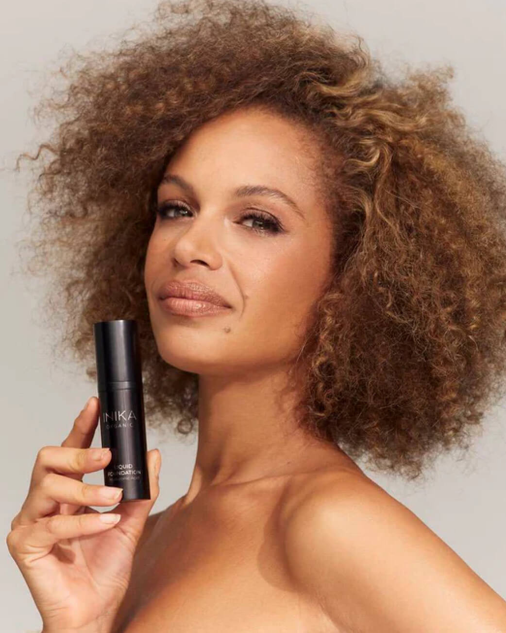Woman with curly hair holding INIKA foundation product.