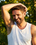 Man smiling against a blurred green background with his arm lifted up.