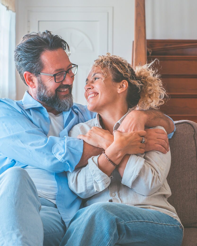 Man and woman sitting together on a couch, smiling and embracing.