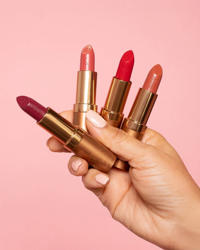 Hand holding four lipsticks against a pink background