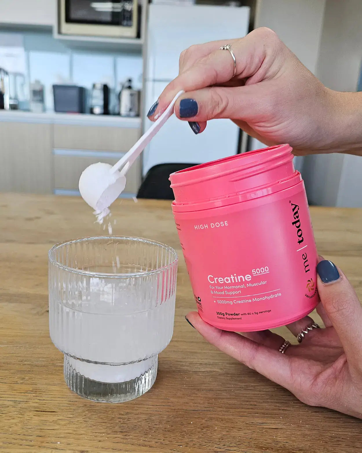 Hand using a plastic scoop to put Me Today Creatine into a glass.