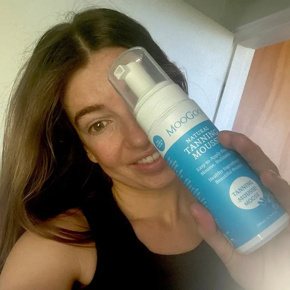 Woman holding up a bottle of Moogoo Natural Tanning Mousse.