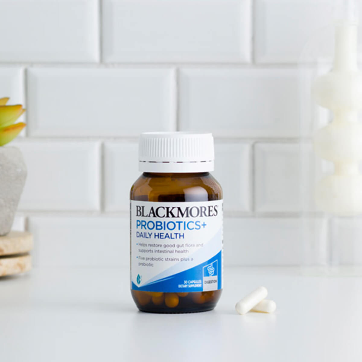 Blackmores Probiotics+ bottle on a kitchen counter with a white tiled wall background.