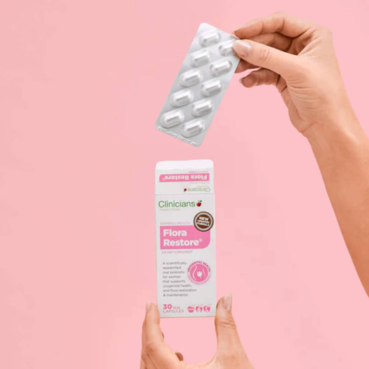 Hand holding a packet of 'Clinicians Flora Restore' capsules against a pink background.