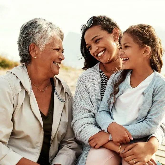 Three generations of women sitting together and smiling outdoors.
