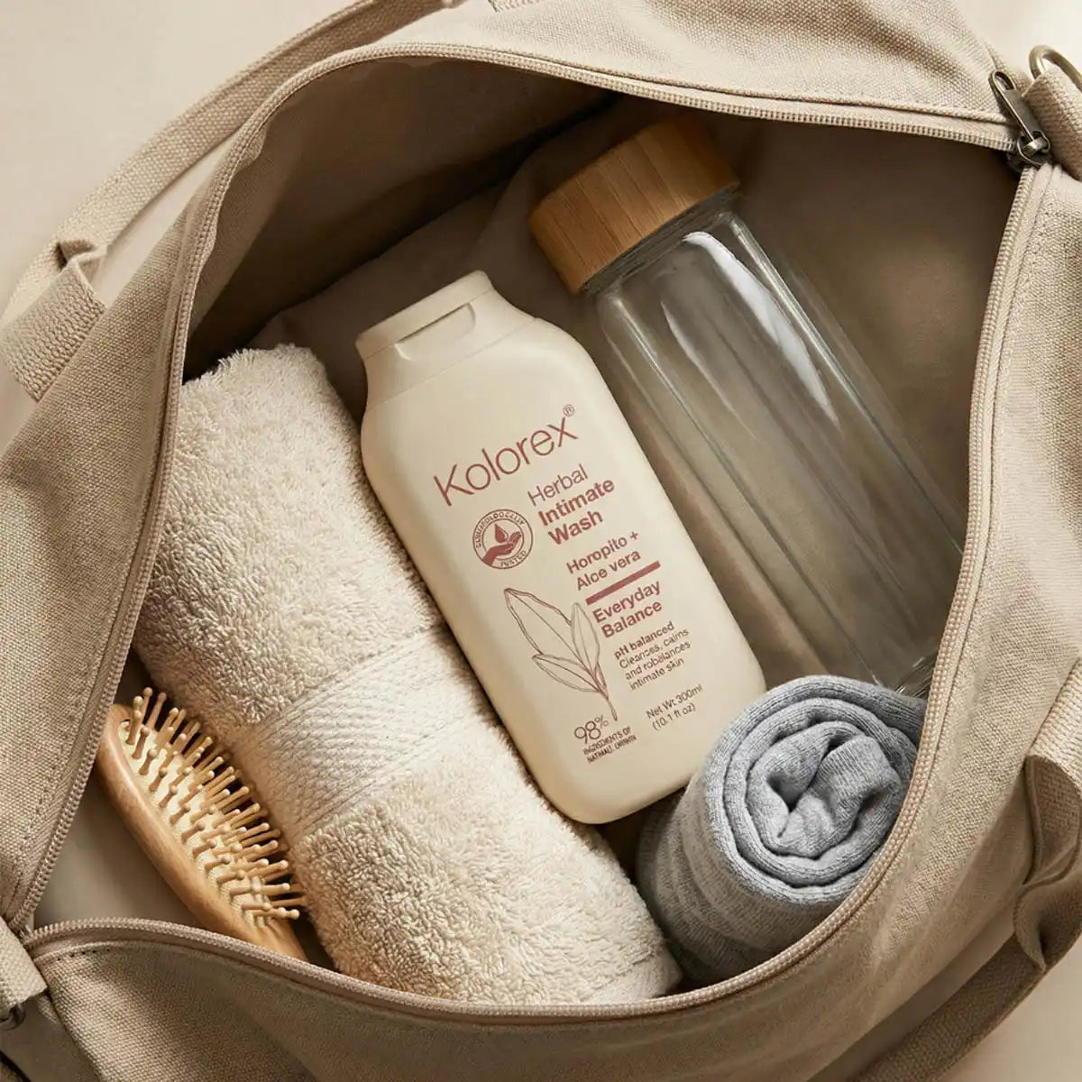 Open beige bag containing a bottle of Kolorex intimate wash, a towel, a brush, and a folded cloth.