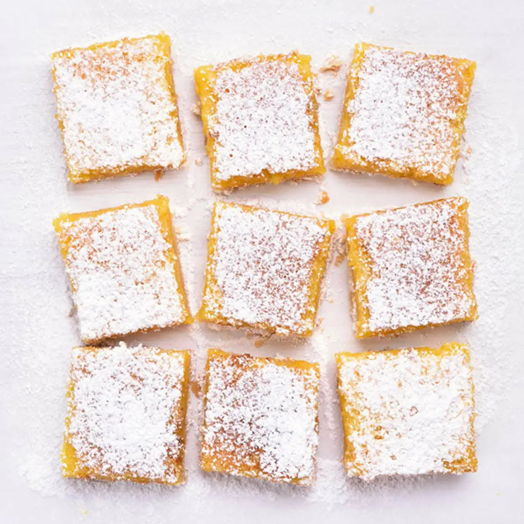 Square lemon bars dusted with powdered sugar on a white surface