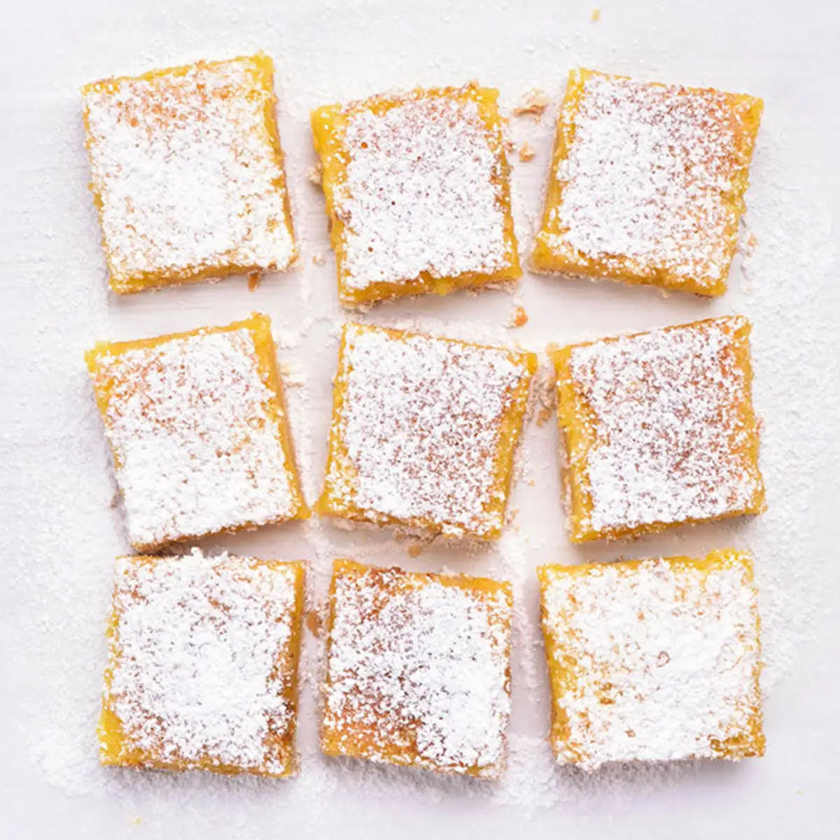 Square lemon bars dusted with powdered sugar on a white surface