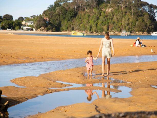 Mother and daughter holding hands as they walk along a beach at low tide.