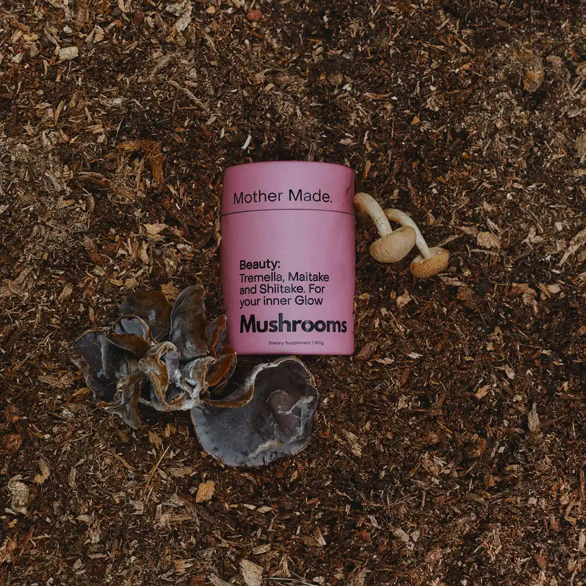 Pink container labeled 'Mother Made' on a dark, textured surface with mushrooms.