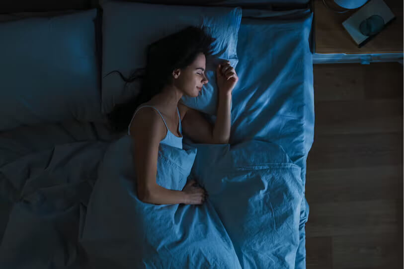 Woman sleeping soundly in bed with blue linens.
